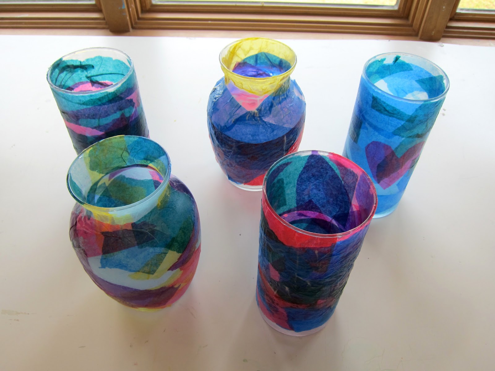 Several glass vases with multi-colored tissue paper decoupaged on so as to produce a stained-glass effect.